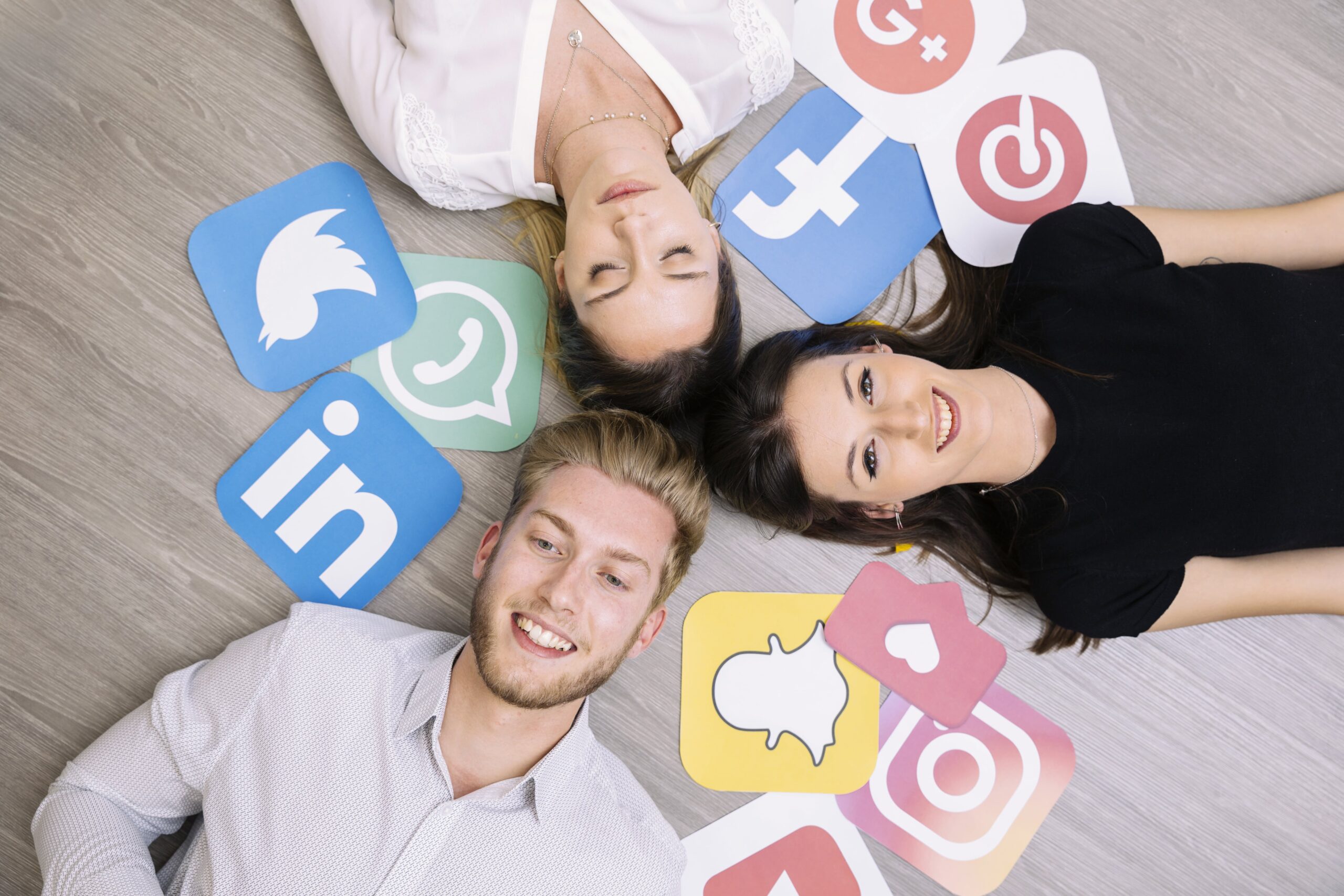 Three young people lying on the floor surrounded by social media icons, including Facebook, Instagram, Twitter, LinkedIn, and Snapchat.